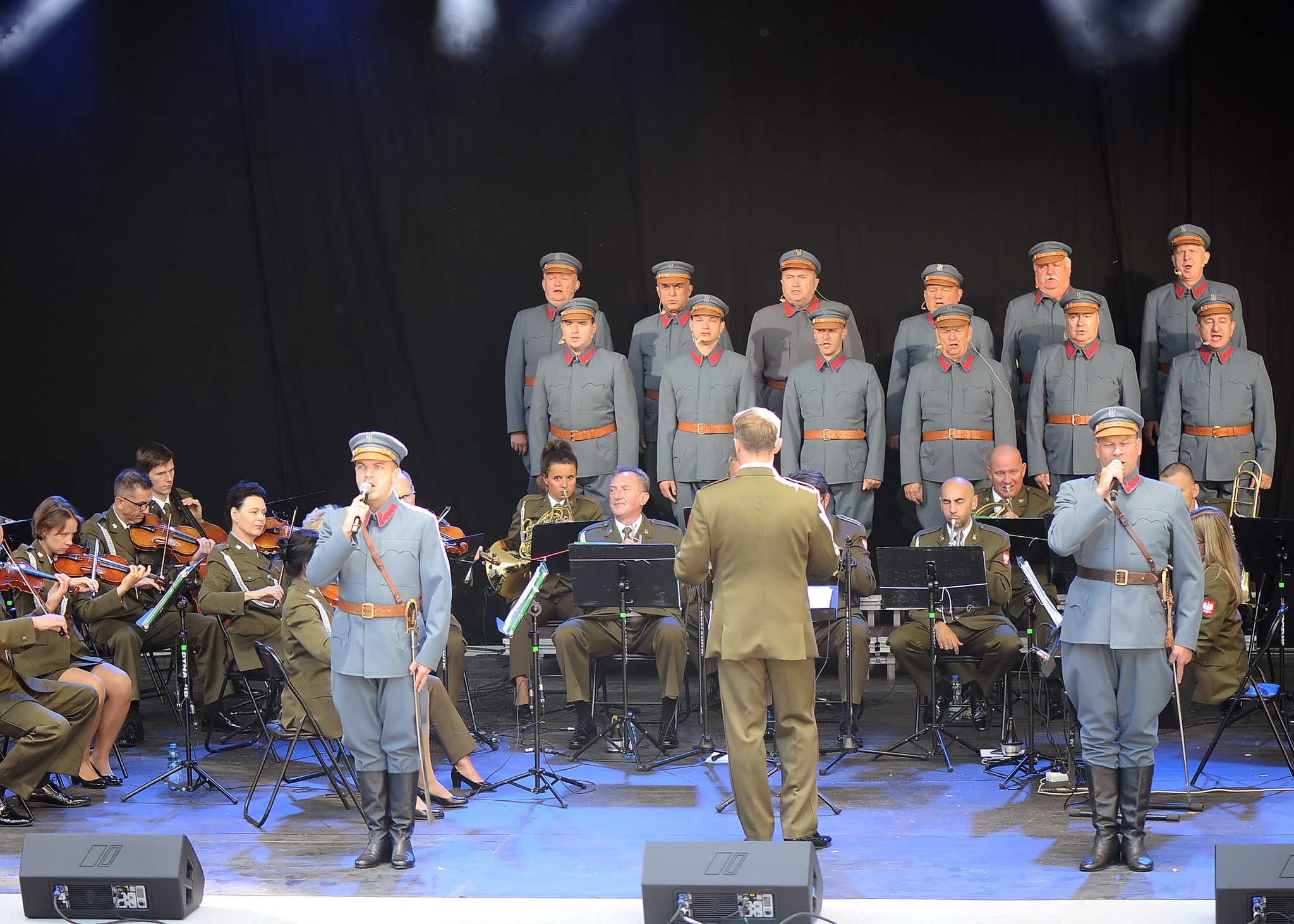 Zdjęcie przedstawia artyst&oacute;w zespołu, ubranych w&nbsp;wojskowe stroje. Jedni grają na&nbsp;instrumentach, inni śpiewają.